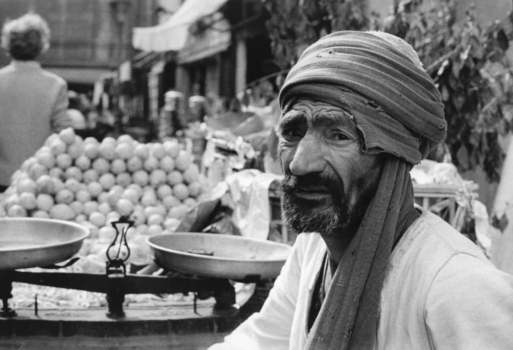 #47 A fruit wither in front of its scales at a stand in the Khan El Khalili bazaar in Cairo, 1972