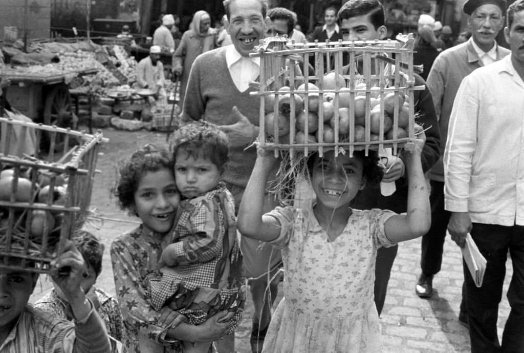 #53 A girl carries a woven basket with fruit on her head to a stall at a bazaar in Cairo, 1972