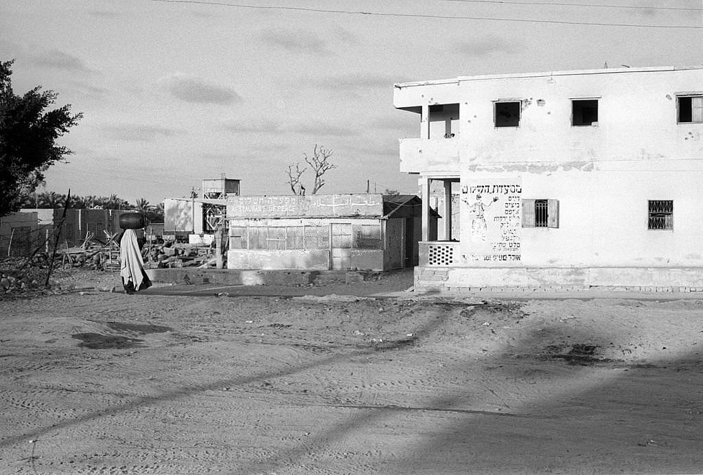 #77 An Egyptian woman transports a water cistern on her head in a desolated background of the war passage, 1973
