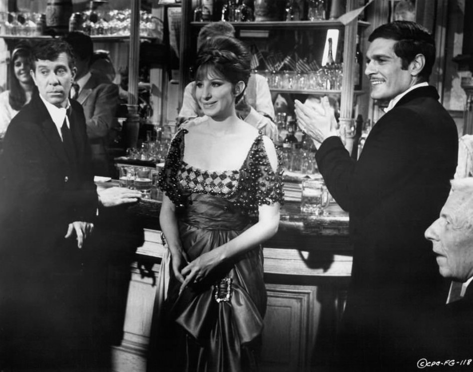 Lee Allen, Barbra Streisand, and Omar Sharif stand at a bar in a scene from the film ‘Funny Girl’, 1968.