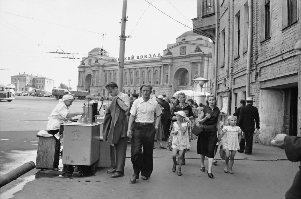 #56 A man holds his jacket as he is served by a street vendor as pedestrians walk by a street in Kyiv, 1965