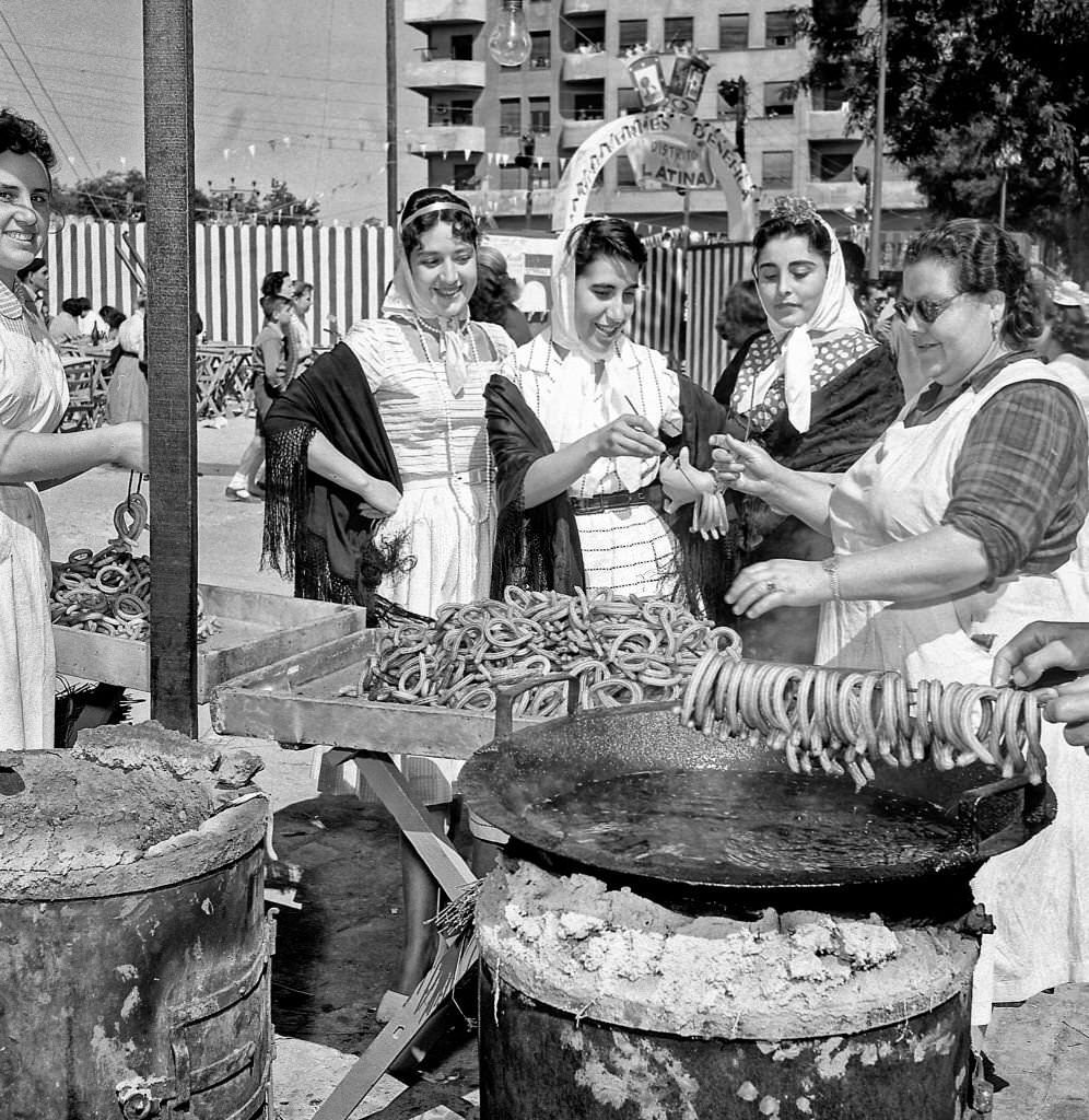 #85 Women dressed as chulapas buy churros from a street stall in San Antonio de la Florida during the 1960s in Madrid, Spain.