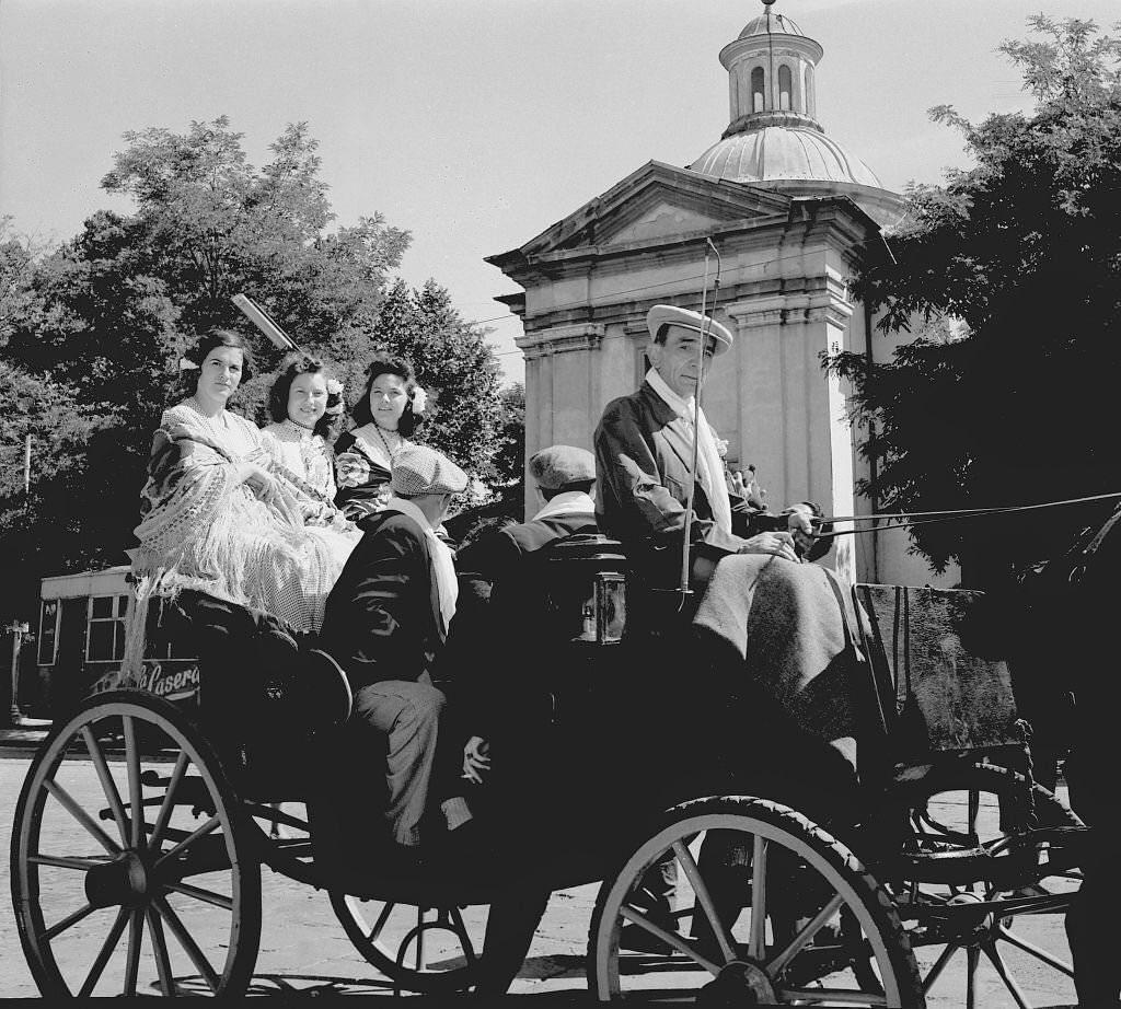 #89 Several women ride in a horse-drawn carriage next to the Hermitage of San Antonio de la Florida, in Madrid during the 1960s.