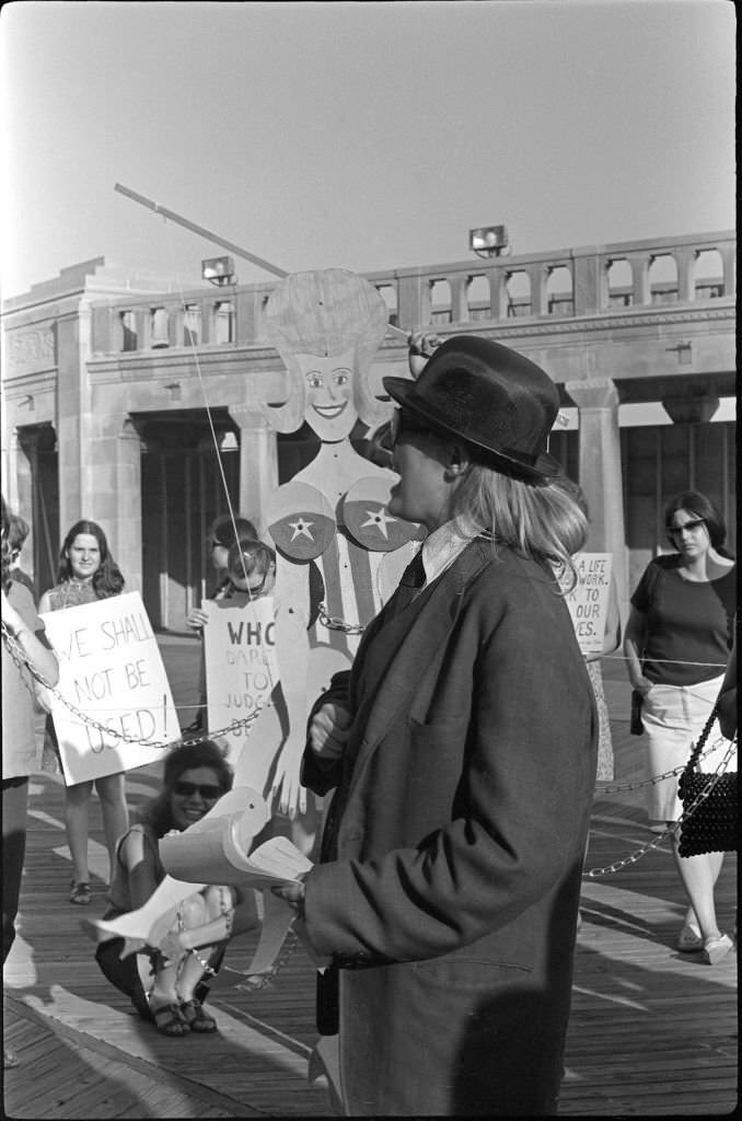 #23 Demonstrator Peggy Dobbins (in coat and hat) ‘auctions’ a chained marionette during a protest of the Miss America beauty pageant, Atlantic City, 1968.