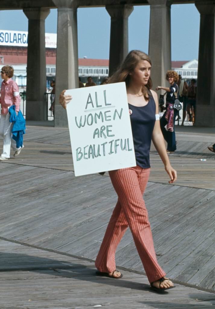 #7 A protest against the Miss America Pageant at Atlantic City, New Jersey, 6th September 1969. A woman walks past with a sign reading ‘All women are beautiful’.
