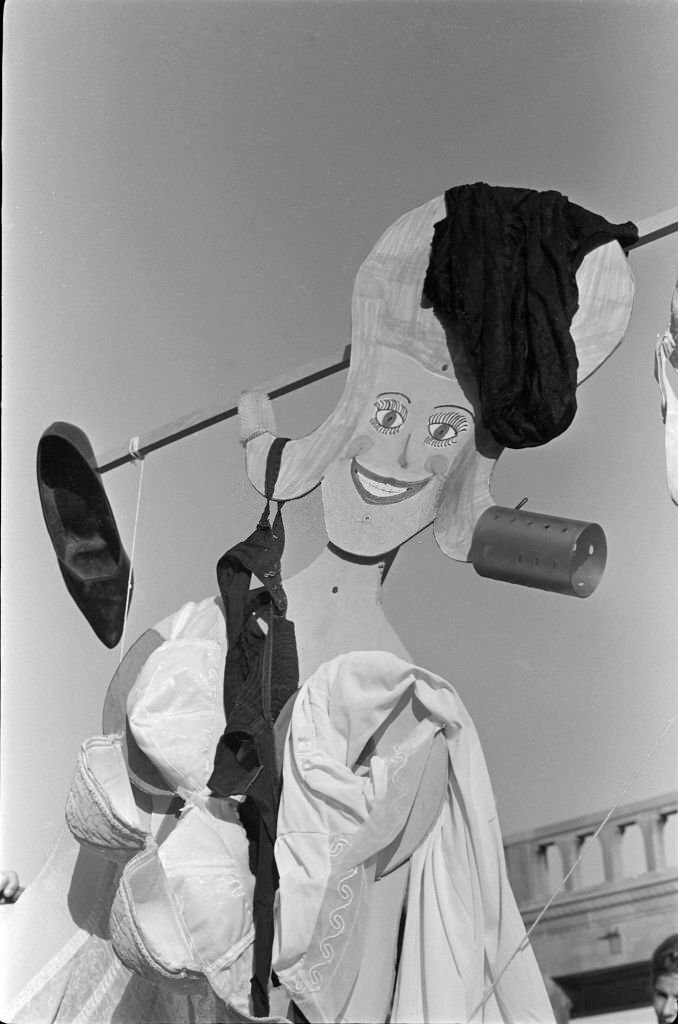#33 A Miss America marionette draped in underwear, high heels, and hair curlers during a protest of the Miss America beauty pageant on the Atlantic City Boardwalk, Atlantic City, 1968.