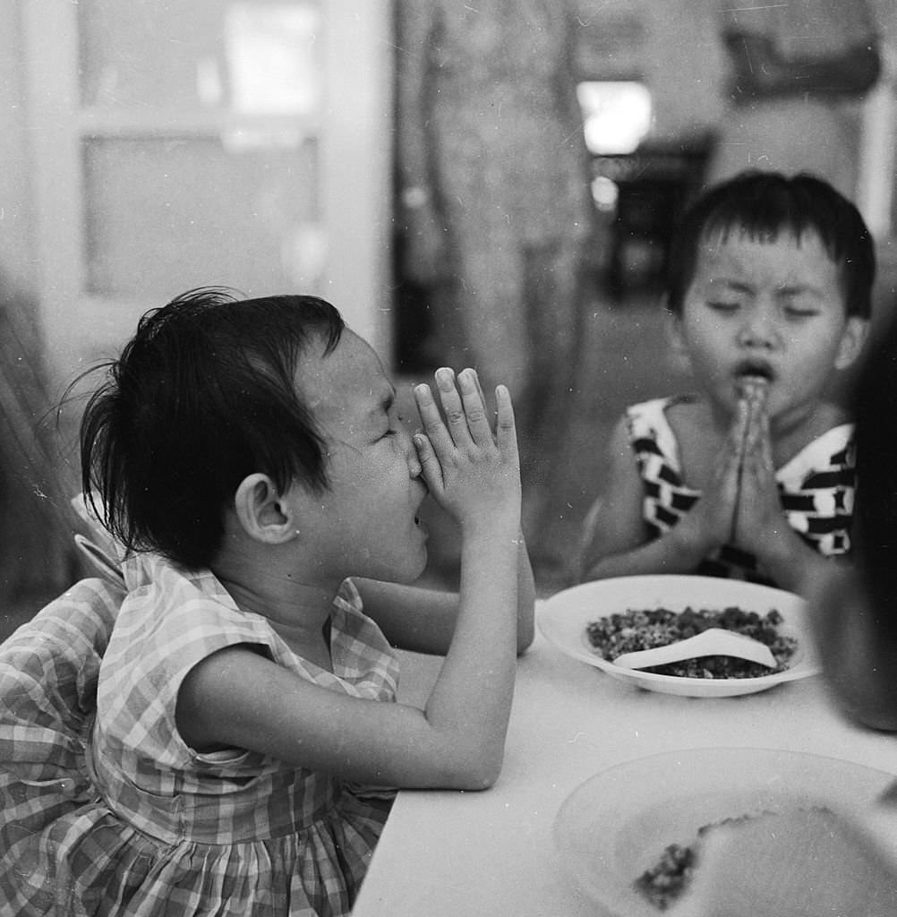 #24 A young girl prays before eating her meal at a Red Cross run school for disabled children in Singapore, 1964
