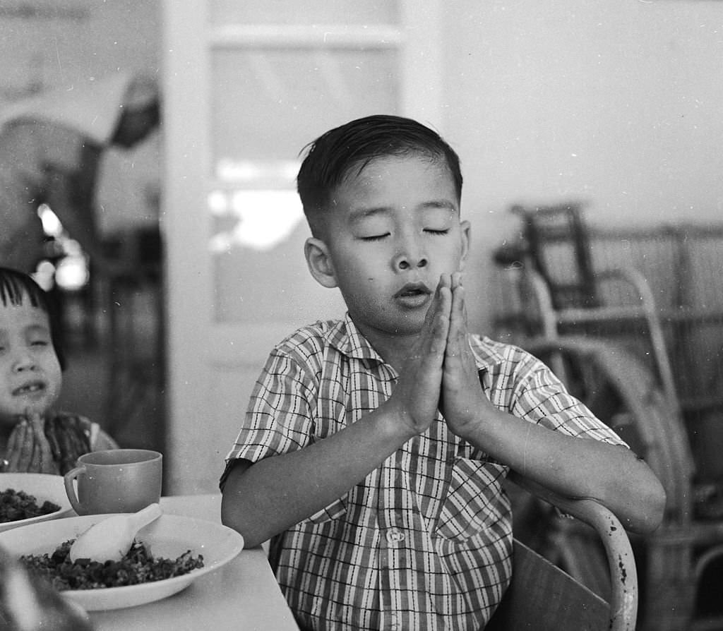 #25 A young boy prays before eating his meal at a school for disabled children in Singapore, run by the Red Cross, 1964