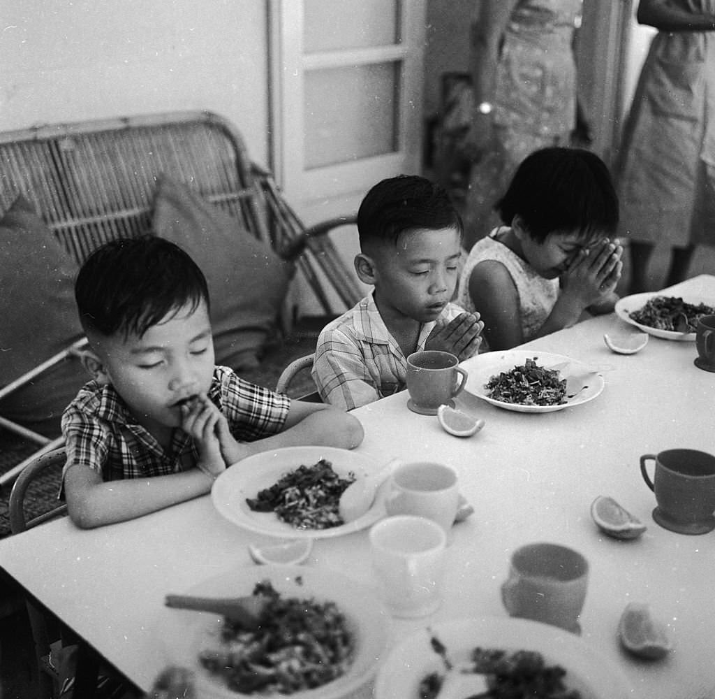 #27 Three children in Singapore in prayer before a meal at a Red Cross school for disabled children, 1964