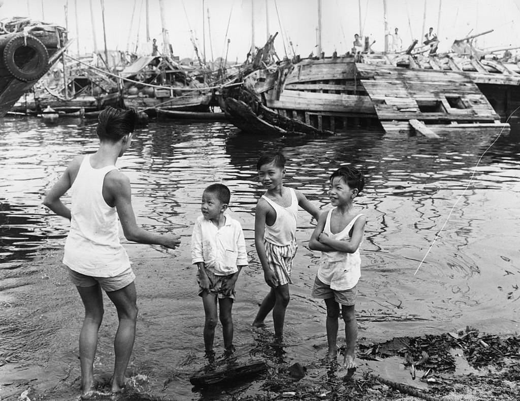 #29 Singaporean children play in the harbour, while behind them there is little activity on the boats, 1963