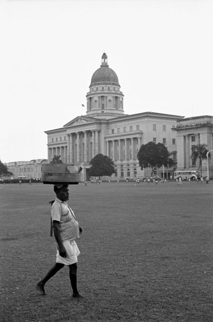 #91 Man carrying items on the head at the park nearby the Old Supreme Court of Singapore, 1962
