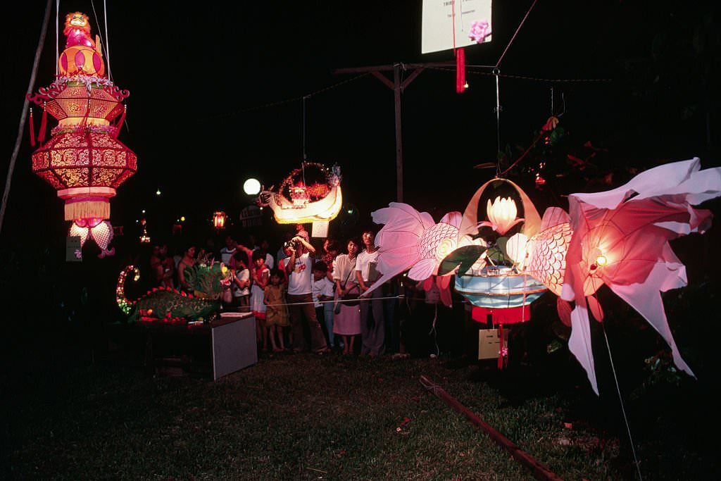 #69 Several onlookers examine paper lanterns shaped like dragons, fish, boats, and other things at a paper lantern festival in Singapore.