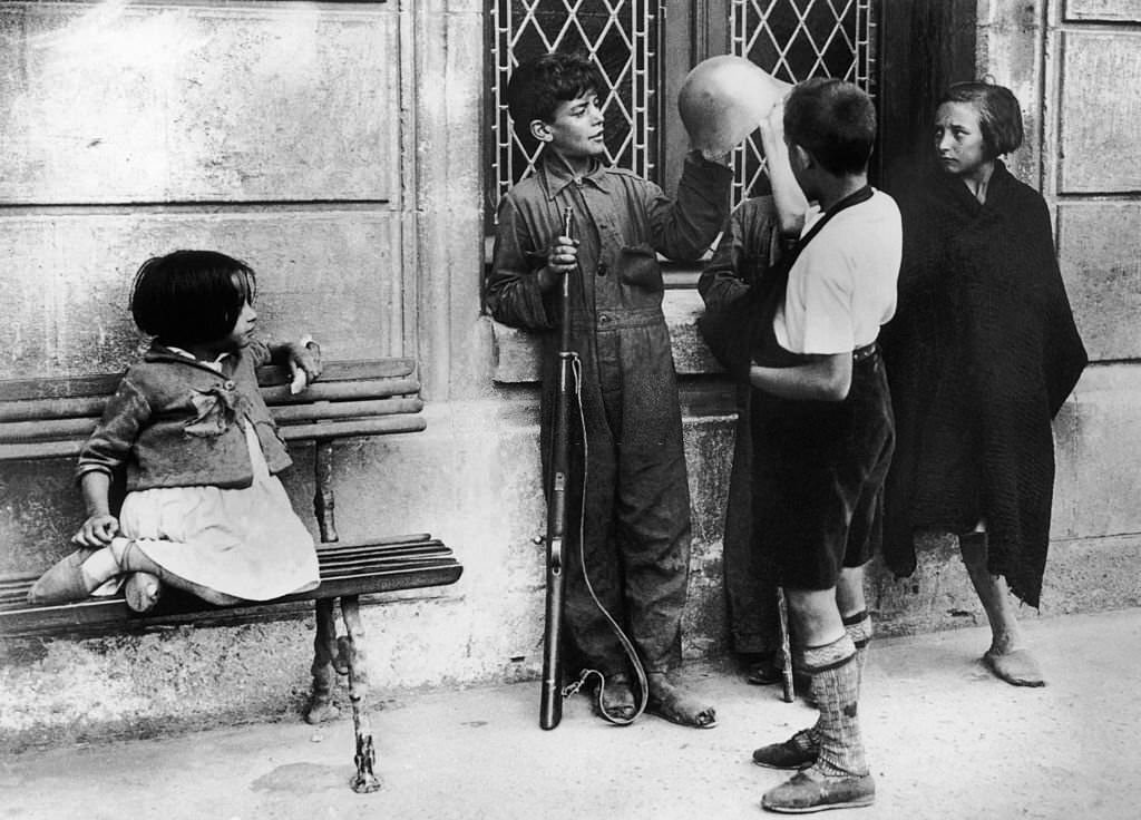 #106 In Burgos during the Spanish civil war, children are admiring the helmet and rifle of the elder brother, signed-up in Franco’s troops.