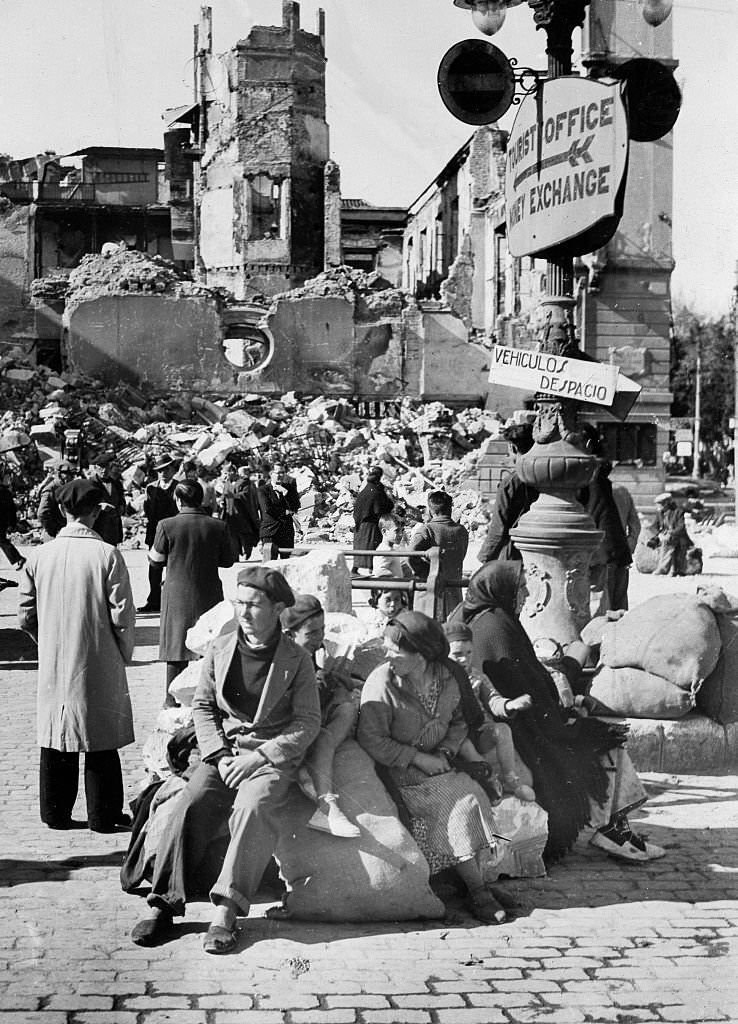 #82 Spanish Civil War Refugees sitting on their belongings in front of a ruined building after the capture of the city by the Nationalists on 7 February 1937