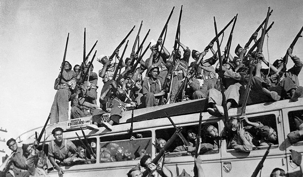 #94 At the Extremadura Front in Spain, a bus full of Republican militiamen waving their arms leaves for the front line. They are for the most part aiming at the sky.
