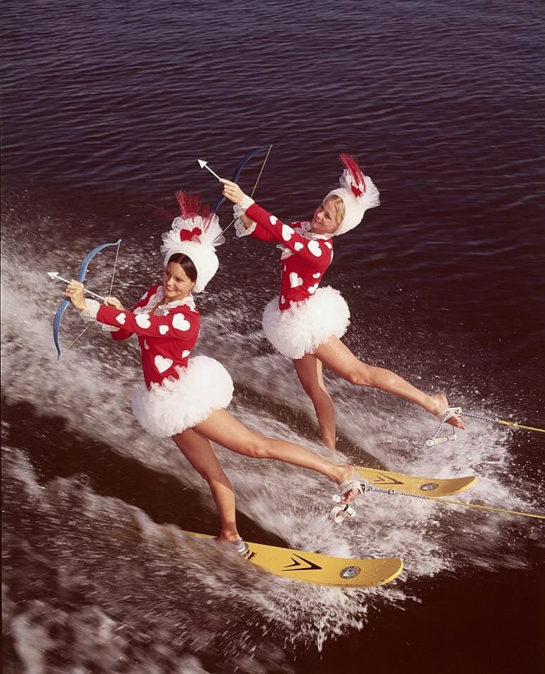 #117 Two pretty cupids take to the water in search of their Valentines at Cypress Gardens, Florida. They’re performing a difficult backward on their water skis as they aim for their sweethearts