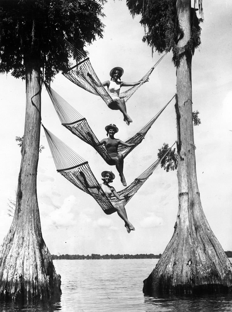 #136 Three sunbathers balance in three hammocks suspended high up above the water in Cypress Gardens, Florida, 1966