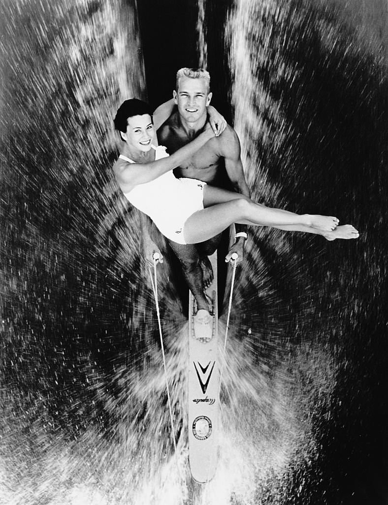 #142 Champion skier Buster MacCalla carries his wife Betty Howard MacCalla in his arms whilst waterskiing on a single ski in Cypress Gardens, Florida, 19th July 1965.