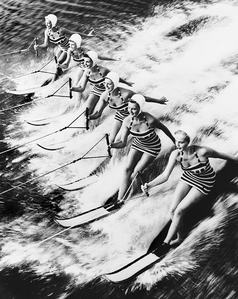 #159 These young women sliding together on water in Cypress Gardens, Florida, where visitors could attend water shows, especially water-skiing exhibitions.