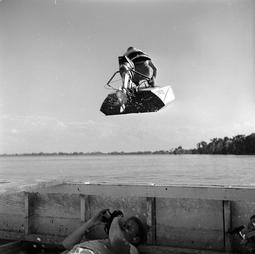 #16 A photographer lies in the bottom of his boat in order to capture an action shot of a speedboat flying overhead, at the Cypress Gardens race course, Florida, 1956
