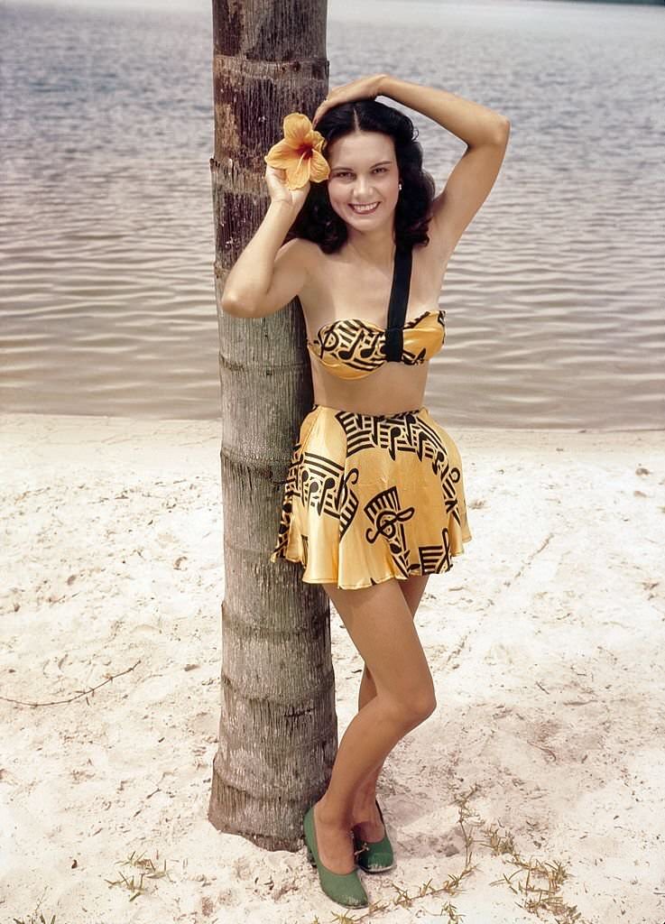 #87 A southern belle model poses by a Palm tree on the beach at Cypress Gardens theme park in 1953 near Winterhaven, Florida.