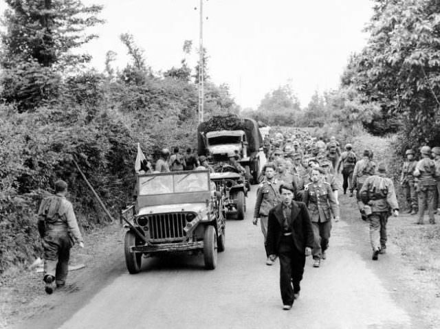 #19 American troops moving up to the front lines, right, pass a long line of German prisoners marching back to a holding camp prior to being shipped out of France, on June 12, 1944.
