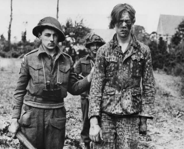 #32 A wounded German prisoner, wearing a camouflages uniform, is escorted to an allied first aid station in France on June 21, 1944