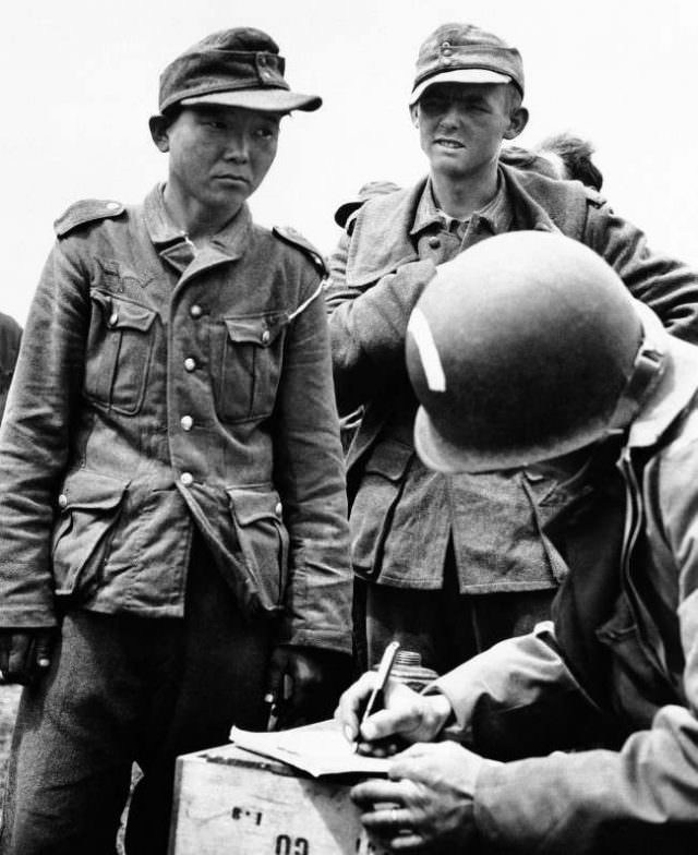 #33 This Japanese, captured while serving in the German army in France on June 21, 1944, gives his name and serial number to an American as he files along with other German prisoners rounded up in the Normandy coast area.