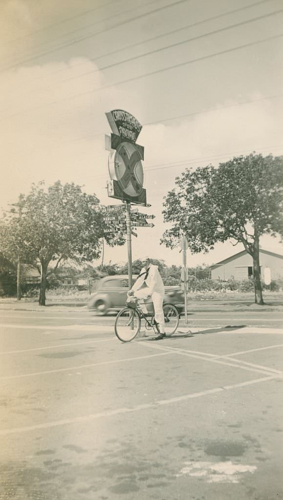 #86 Sailor on bicycling in front of Crossroads of the Pacific sign, 1940s