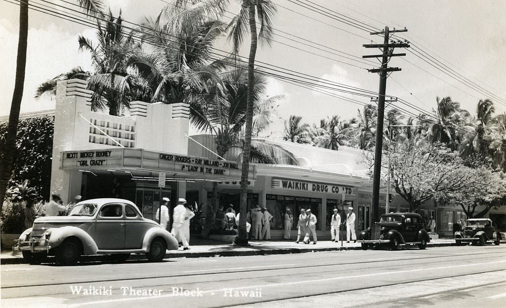 #94 Sailors mill outside of Waikiki theater block on quiet street with parked cars and palm trees, 1940s
