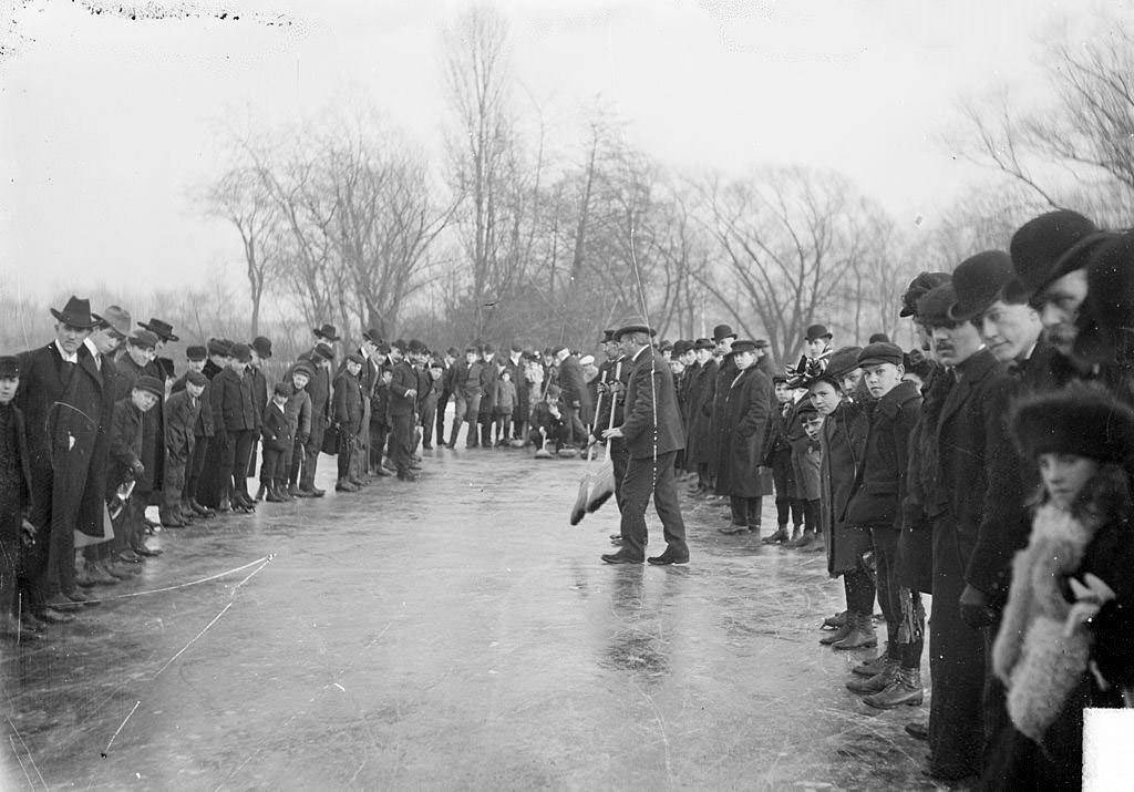 #159 Two men with brooms standing on the ice amidst spectators in a curling match at Jackson Park in Chicago, Illinois, 1903.