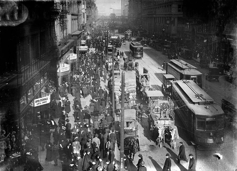 #208 Shoppers on State Street, with a streetcar approaching curved track and a two-horse team pulling a wagon in the foreground, Chicago, Illinois, 1900s.
