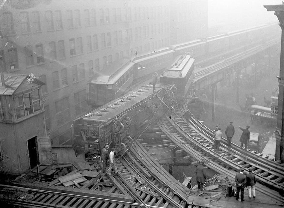 #44 Elevated train wreck, with one train car off its tracks and lying across the adjacent track in front of another elevated train, 1900s.