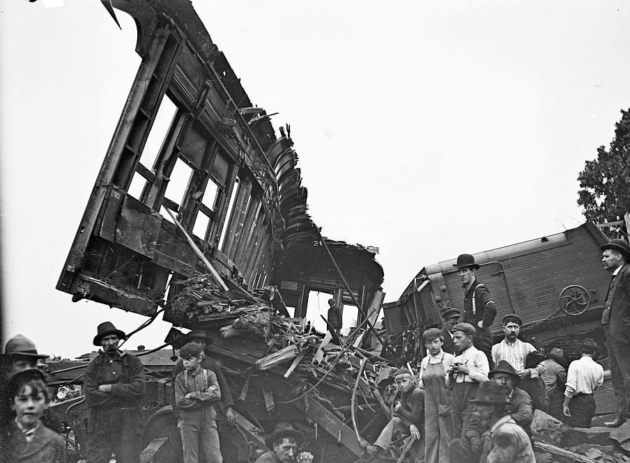 #45 Overturned and damaged train cars from a train accident with men and children standing in front of the wreckage, 1900s.