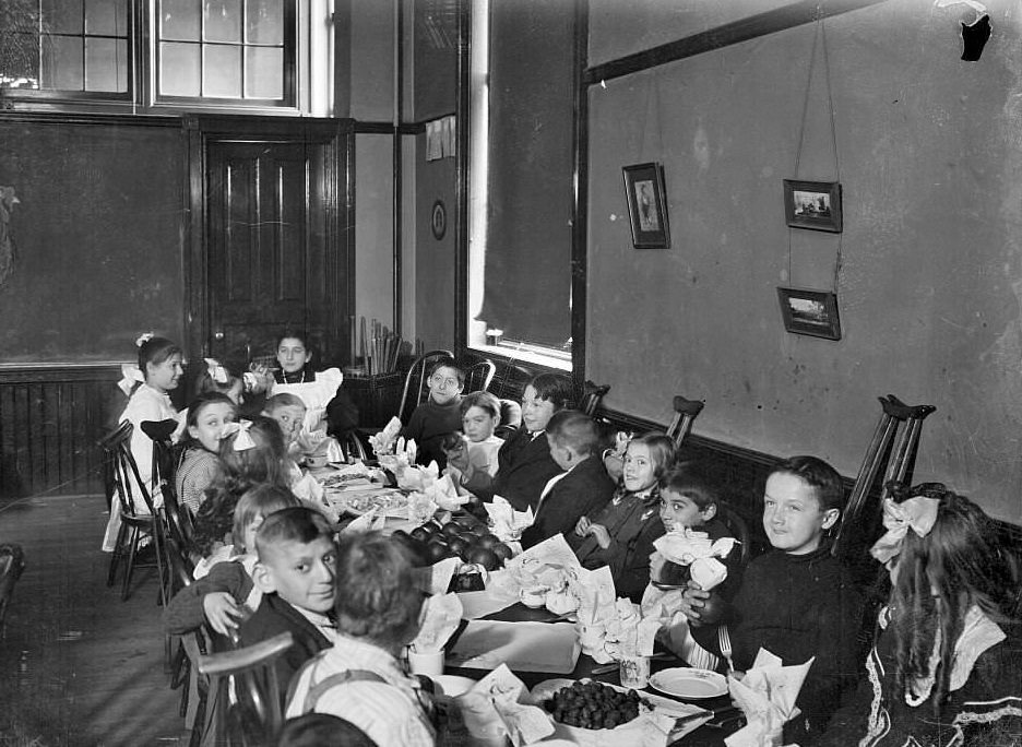 #230 Children with handicaps sitting around a table with food in a classroom, Chicago, Illinois, 1905.