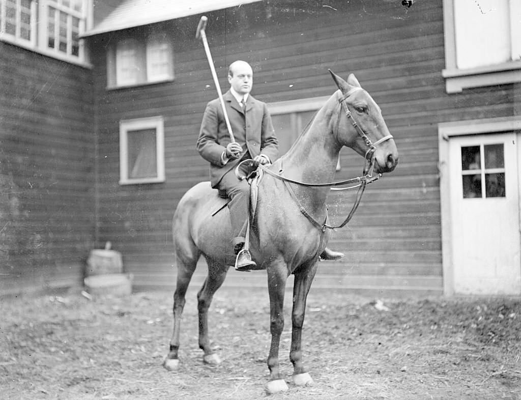 #68 Polo player holding a polo mallet, sitting on horseback in a paddock area in front of a barn in Chicago, Illinois, 1901.