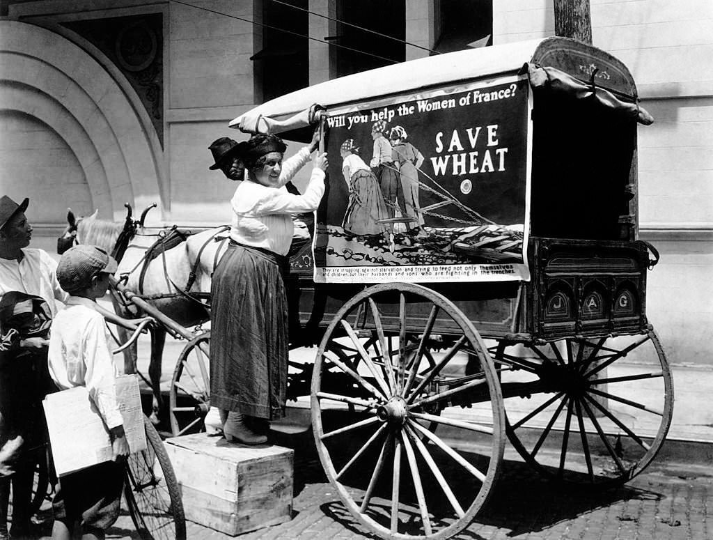 #43 Tacking up a United States Food Administration poster encouraging people to “Save Wheat” and help the women of France during World War One in Mobile, Alabama, 1918.