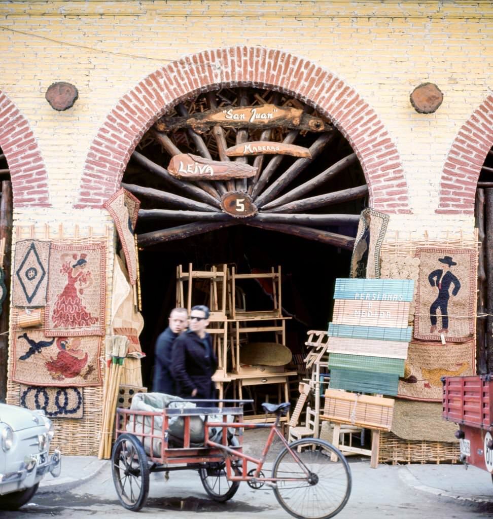 #186 View of pedestrians as they walk past an antiques shop, Malaga, Andalusia, Spain, 1964.