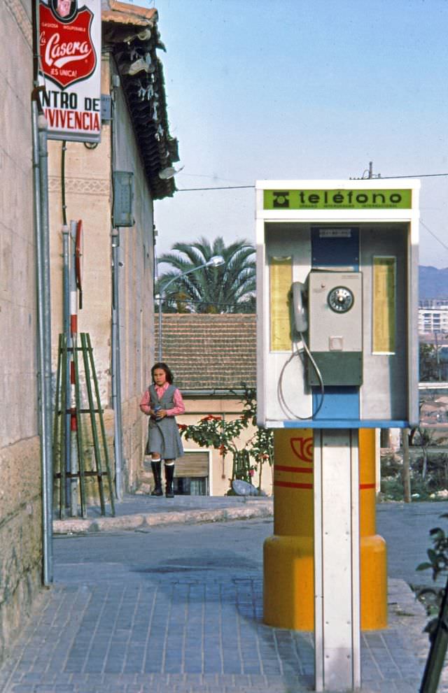 #247 A school girl in her uniform walking towards a mailbox and pay telephone, Barrio Benalúa, Alicante, Valencia, 1977