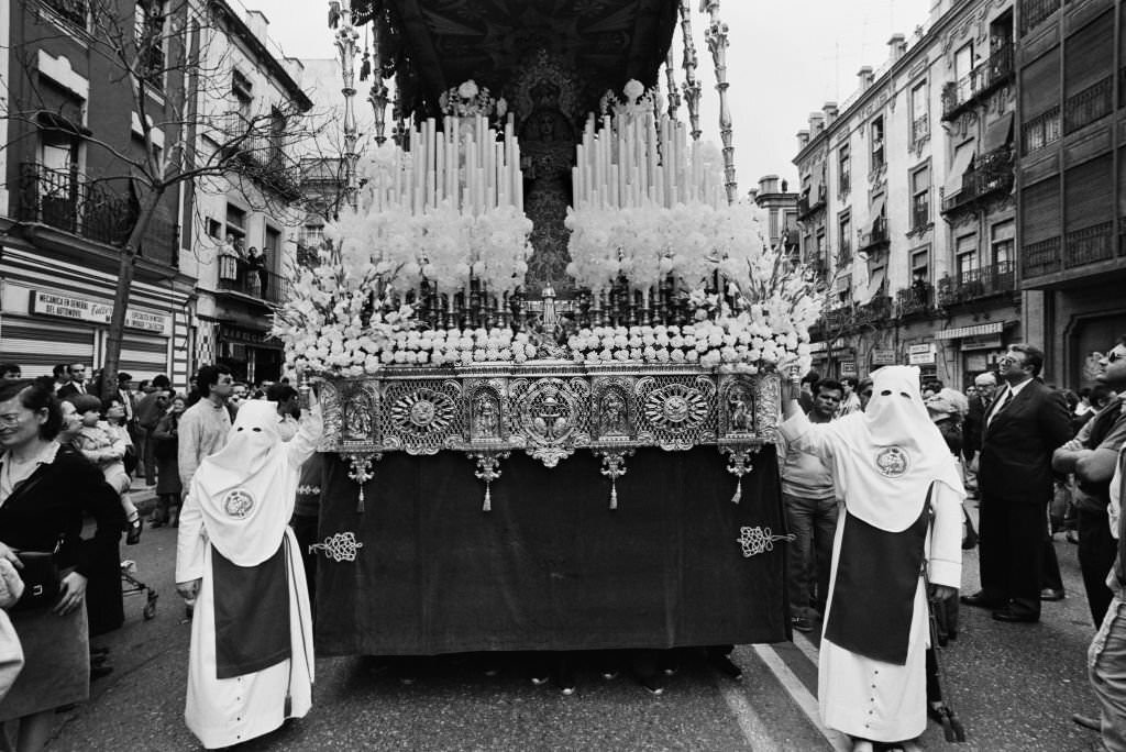 #114 Celebrations for Holy Week (Semana Santa) underway in Seville with hooded penitents, known as ‘Nazarenos’ dressed in their traditional white robes as they prepare to take part in the religious processions through the city of Seville, Andalusia, 1985.