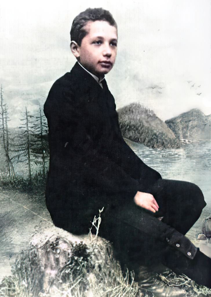 #20 Albert Einstein when he was fourteen years old, wearing a black suit and a calm expression and posing in front of an outdoor backdrop, 1893.