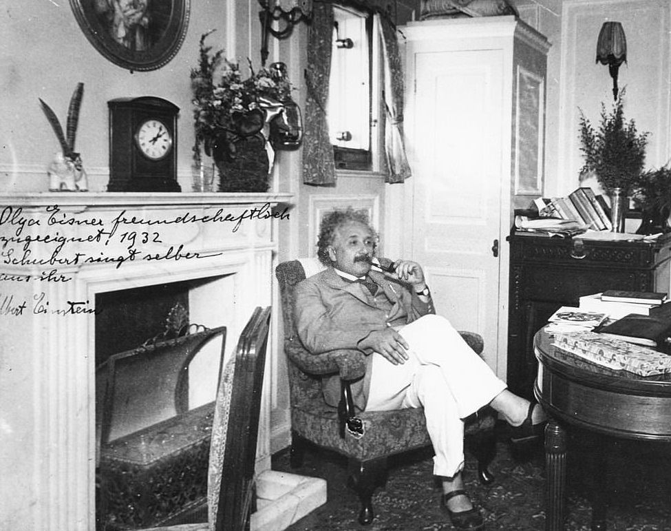 #99 Albert Einstein sitting in an armchair and smoking a pipe, 1932.