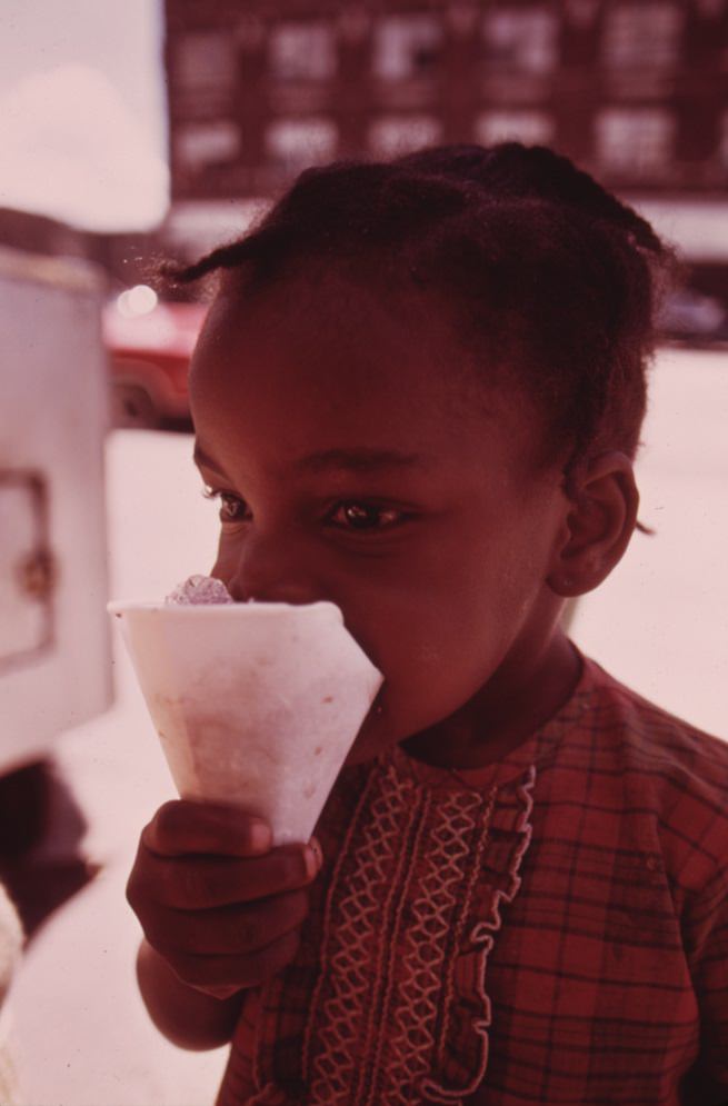 #45 A child savors a snow cone just received from a sidewalk vendor on Chicago’s West Side.