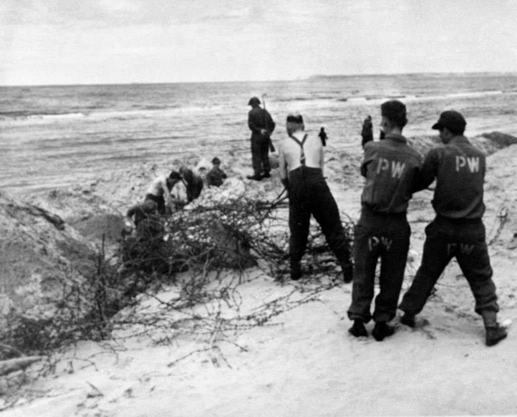 #124 German prisoners of war line under the watch of English soldiers, in Deauville, France in 1946.