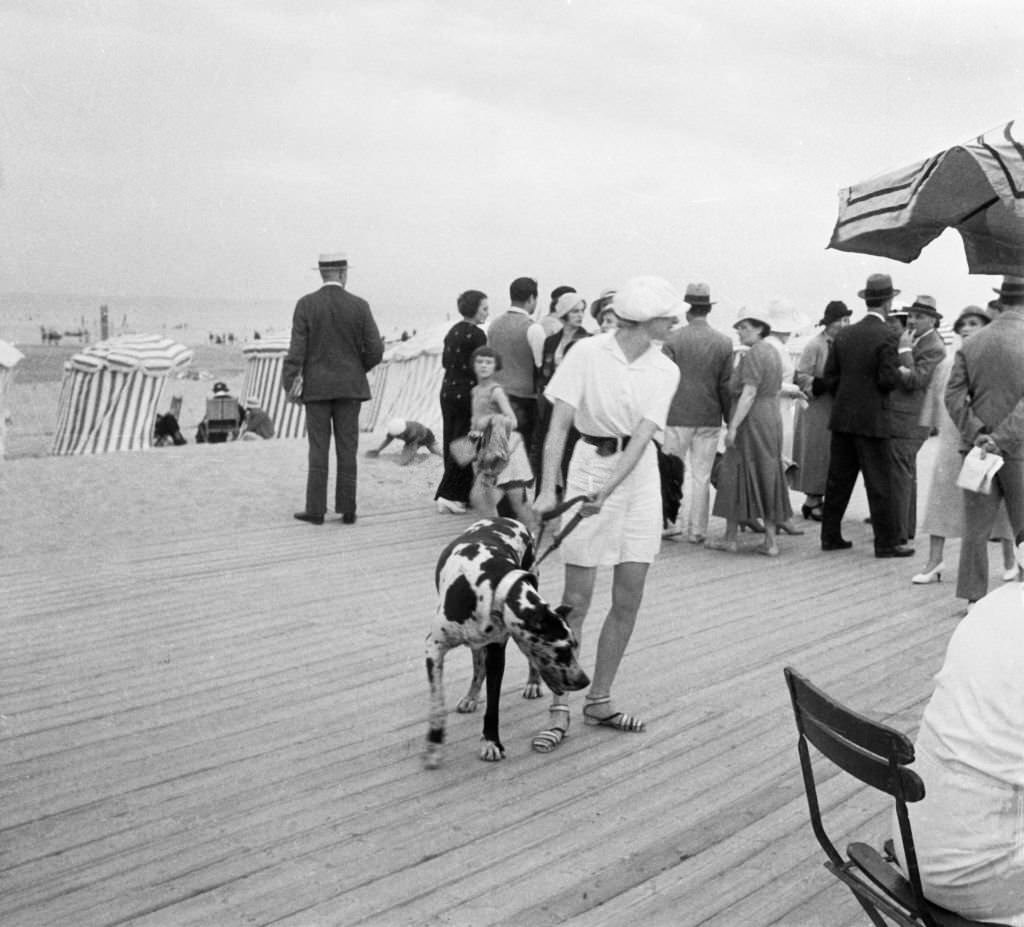 #134 Woman holding her dog on a leash on the planks by the beach, in Deauville, France in 1938.