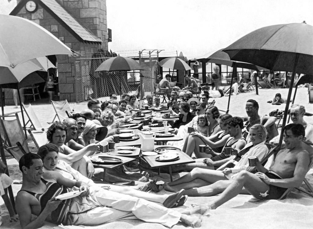 #92 Members of the Deauville Club have their weekly breakfast meetings on the beach after a quick dip in the surf, 1930
