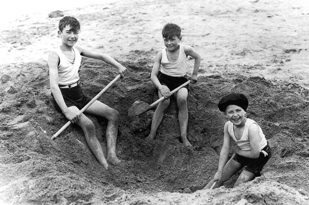 #95 In August 1929, on Deauville beach, these three children dug a hole in the sand with shovels.