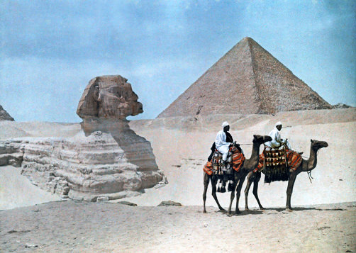#45 Two men on camel-back ride past the Sphinx and Great Pyramid.