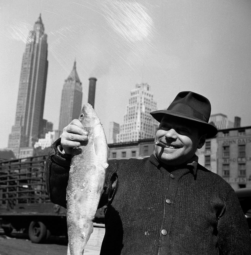 #121 Fisherman holding a fish at the Fulton Fish Market. New York City, 1943.