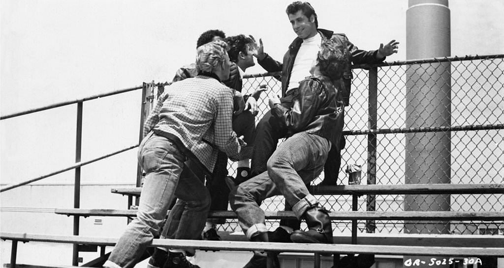 John Travolta with his crew on the bleachers in the ‘Summer Nights’ scene from the Paramount musical, ‘Grease’, 1978.